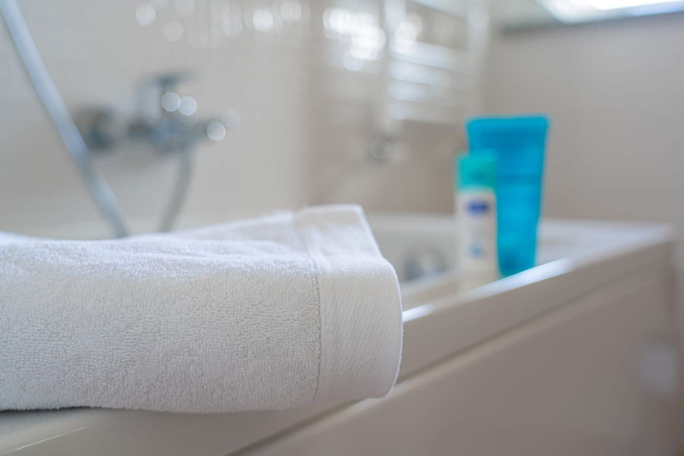 A cotton bath mat in front of a bathtub in a bright bathroom