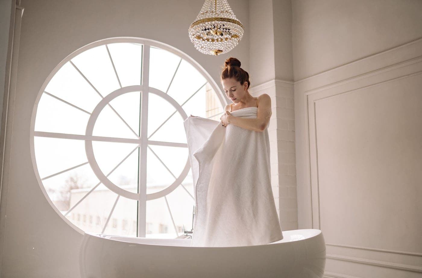 A person wrapped in a large cotton bath sheet beside a bathtub