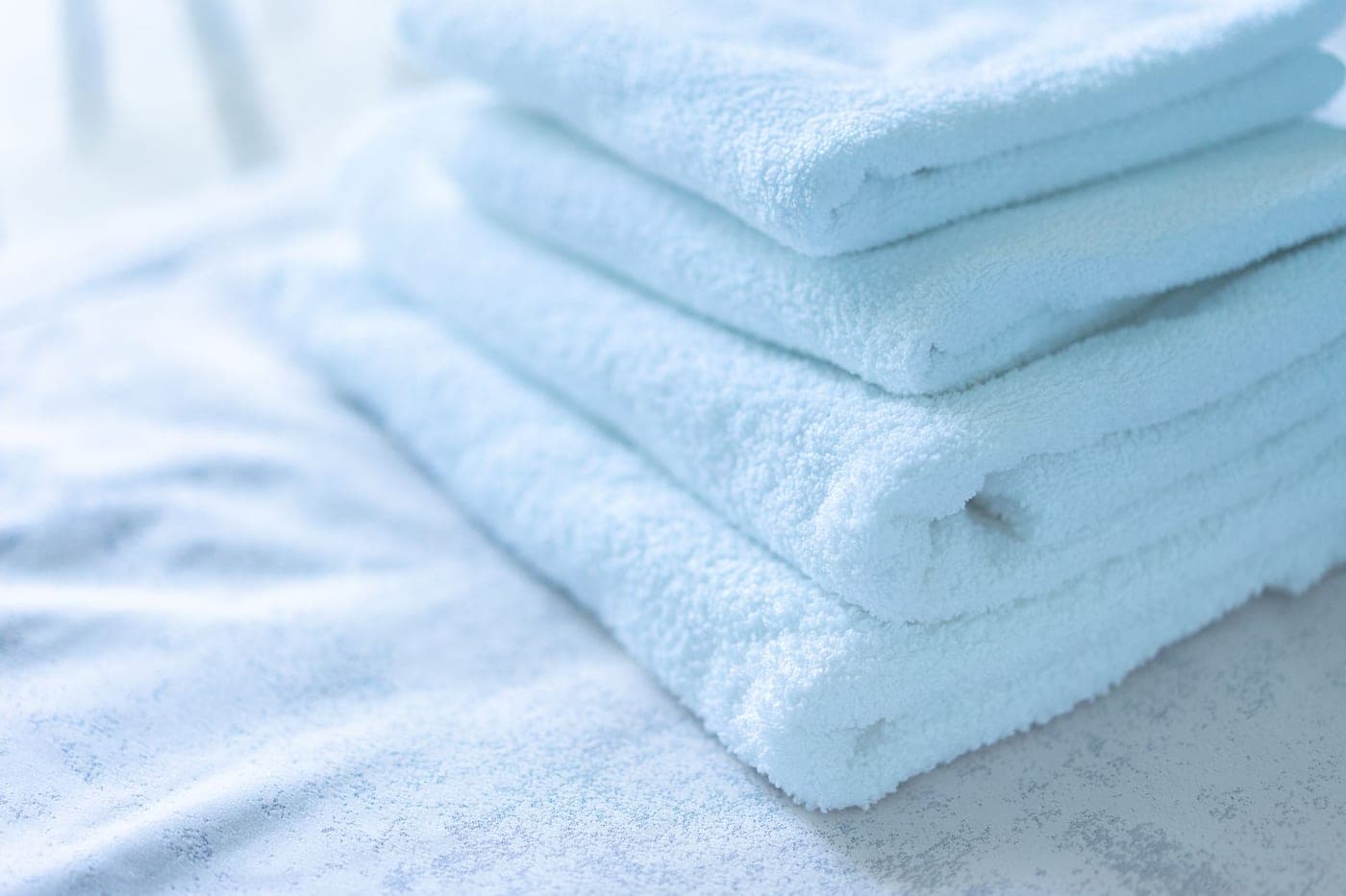 Well-worn but sound white cotton towels folded in a linen cupboard
